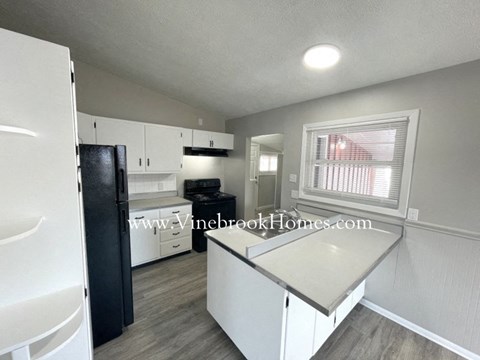 A kitchen with a black refrigerator and white cabinets.
