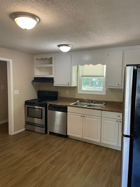 A kitchen with a black fridge, white cabinets, and a wooden floor.