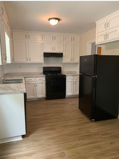 A black refrigerator stands in a kitchen with white cabinets.