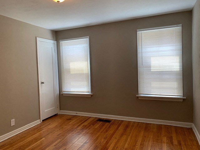an empty room with wood floors and two windows