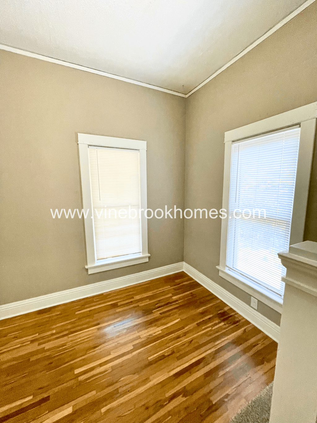 a small bedroom with two windows and a wooden floor