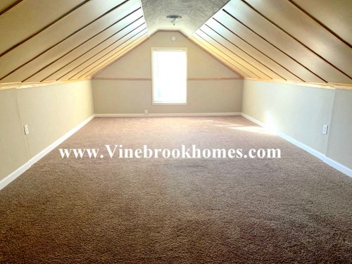 an empty attic with a window and a carpeted floor