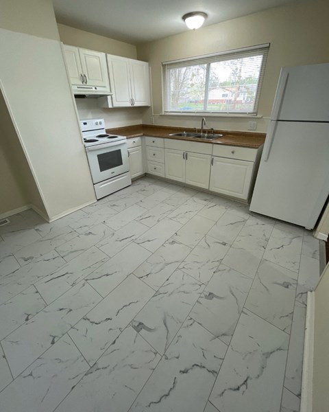 A kitchen with white appliances and marble flooring.