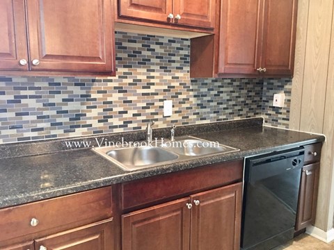 A kitchen with brown cabinets and a black dishwasher.