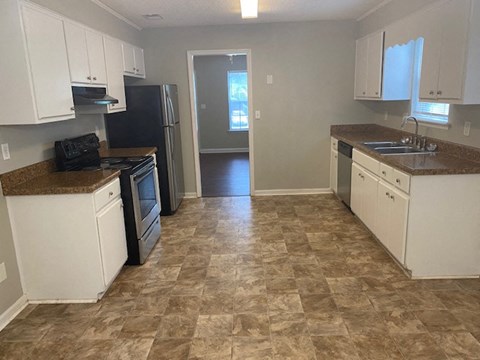 A kitchen with white cabinets and brown tiled flooring.