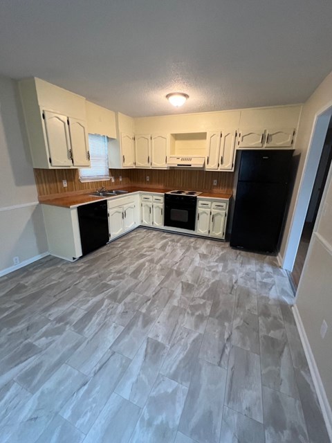 A kitchen with a black refrigerator and white cabinets.