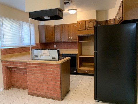 A black refrigerator stands in a kitchen with wooden cabinets and a brick island.