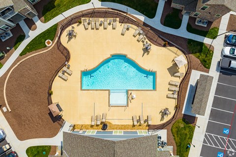 An aerial view of a swimming pool surrounded by a sandy area and a parking lot.