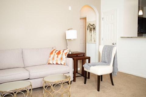 A living room with a grey couch, a chair with a grey blanket, a table with a lamp and a painting on the wall.