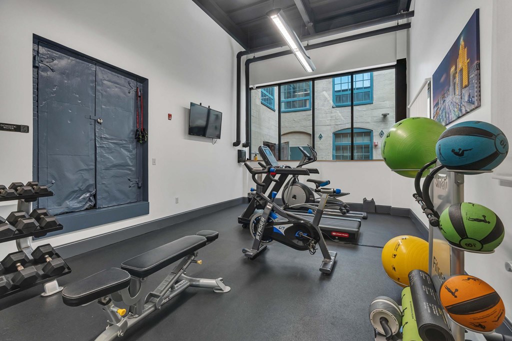A gym with a rowing machine, dumbbells, and exercise balls.
