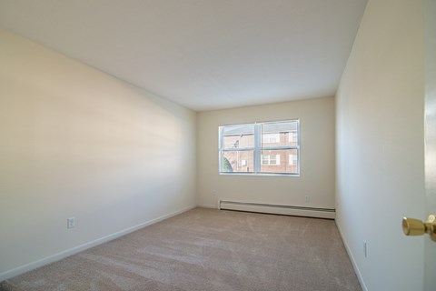 a bedroom with white walls and carpet and a window