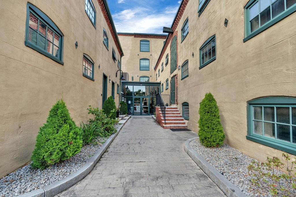 A long, narrow alleyway between two tan buildings with green trim and steps leading to the entrance.