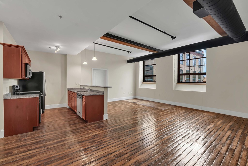 A room with wooden floors and a kitchen area with brown cabinets.