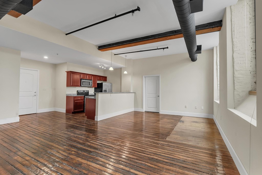 A room with wooden floors and a kitchenette in the corner.