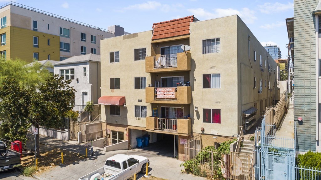 A building with a red tile roof is in the middle of a street with cars parked on the side.