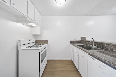 A white kitchen with a stove, sink, and cabinets.
