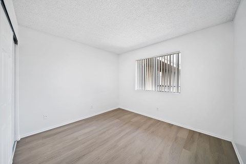 A room with a wooden floor and a window with bars on it.
