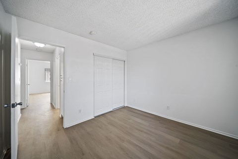 A room with white walls and wood flooring with a door on the left.