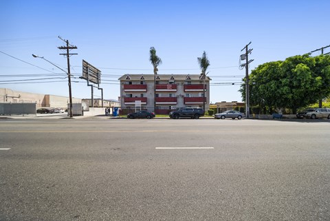 A street view with a building in the background and cars parked on the side of the road.