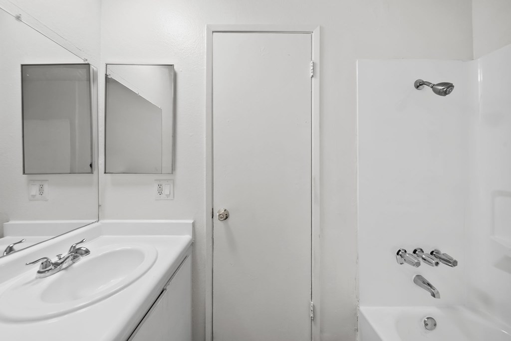 A white bathroom with a sink, mirror, and bathtub.