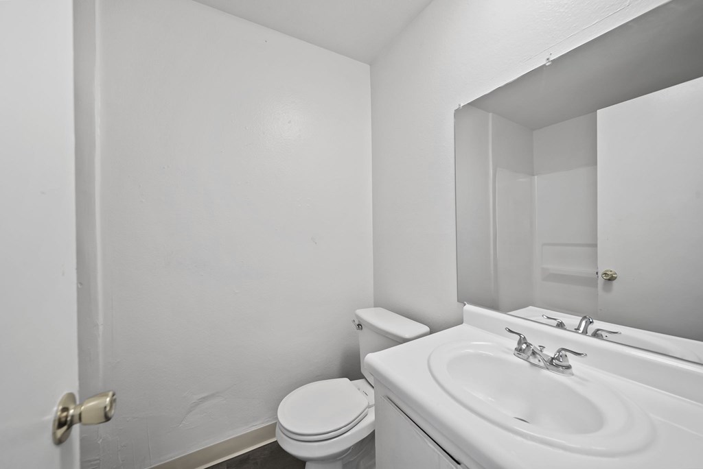 A white bathroom with a toilet, sink and mirror.