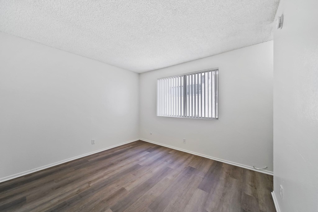 A room with wooden flooring and a window with blinds.