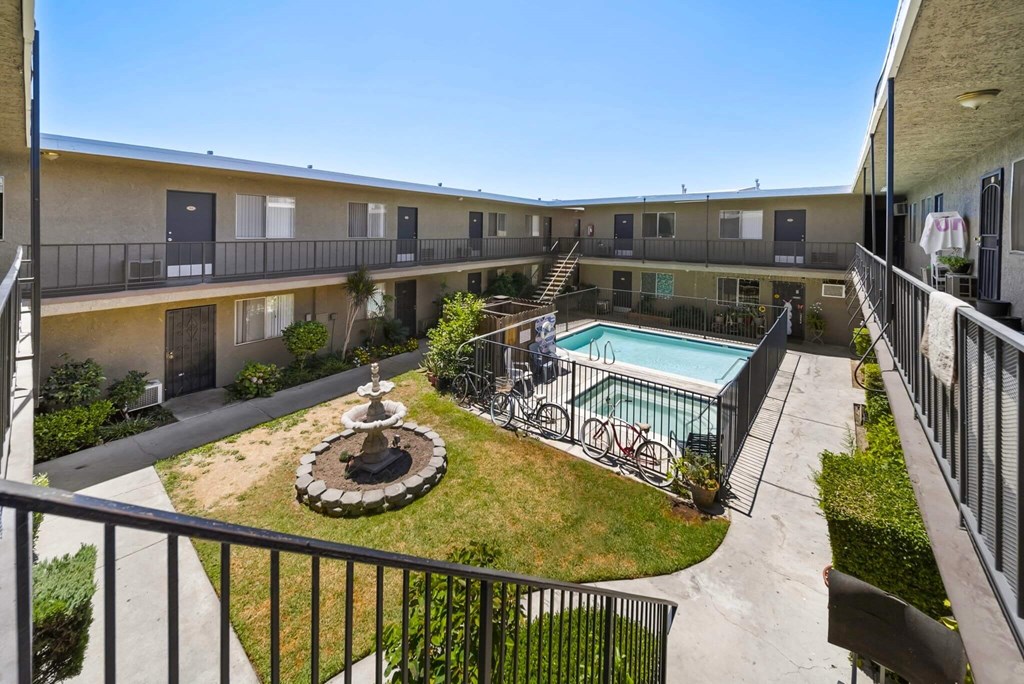 A balcony overlooks a courtyard with a fountain, bicycles, and a pool.