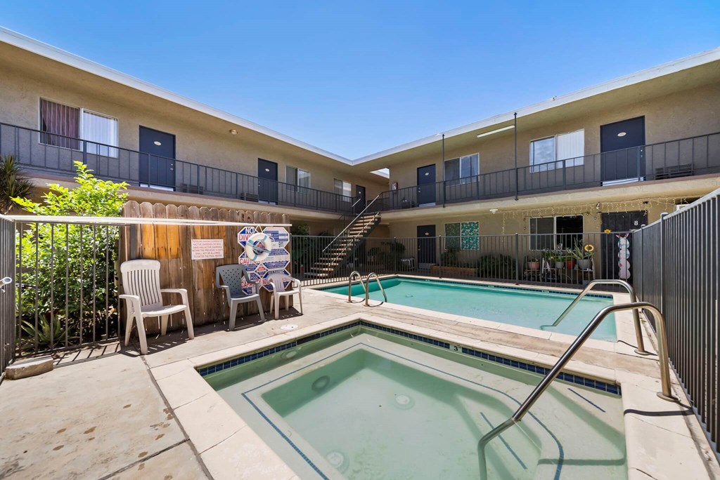 A pool in a courtyard surrounded by chairs and a building.
