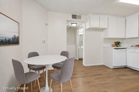 A white dining table with grey chairs in a white kitchen.
