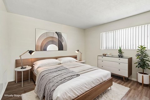 A bedroom with a large bed, a nightstand with a lamp, and a dresser with a plant on top.