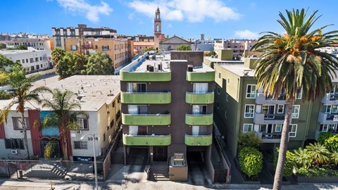 A tall green building with a balcony in the middle stands in front of a red building.