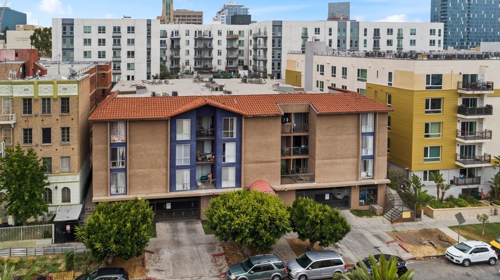 A building with a red tile roof is surrounded by other buildings and has cars parked in front.