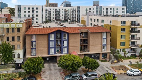 A building with a red tile roof is surrounded by other buildings and has cars parked in front.