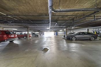A parking garage with a few cars and a puddle on the floor.