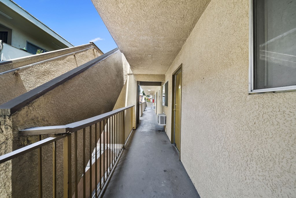 A long, narrow hallway with a metal railing on the left side and a wall on the right side.