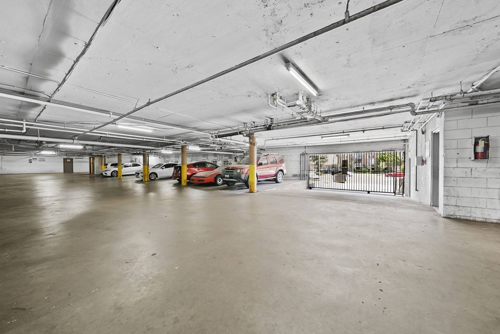 A parking garage with a few cars and a fire extinguisher on the wall.
