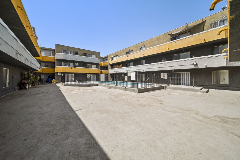 A courtyard surrounded by buildings with a fence and a bird on the ground.
