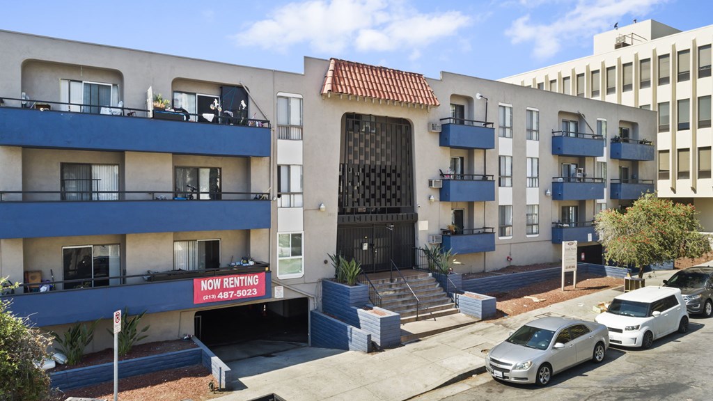 A building with a sign that says "Now Renting" is in front of a car.