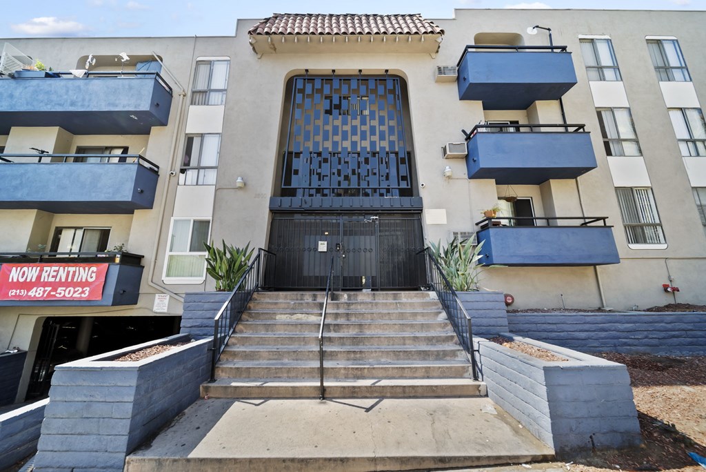 A building with a black gate and a sign that says "Now Renting" in front of it.