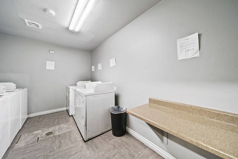 A room with a white washing machine, a black trash can, and a wooden bench.