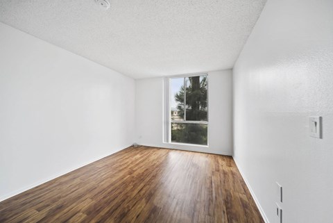 A room with wooden floors and a window showing trees outside.