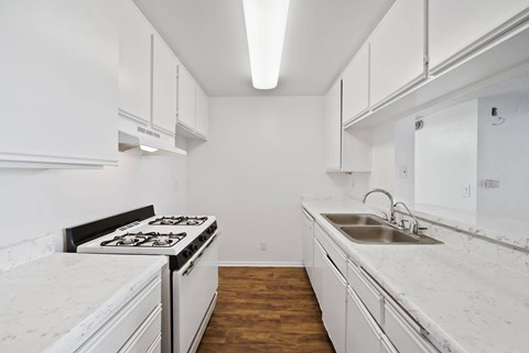 A white kitchen with a stove, sink and cabinets.