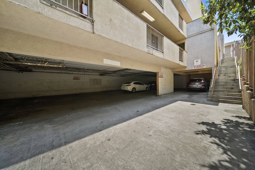 A car is parked in a garage under a building with a staircase on the right side.