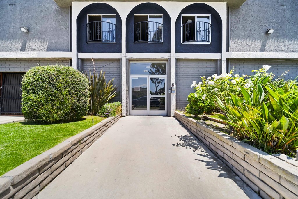 A building with a grey facade and a white door is surrounded by greenery.