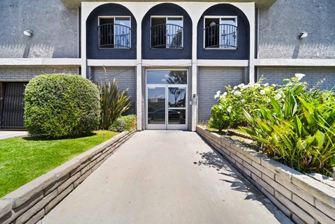 A building with a grey facade and a white door is surrounded by greenery.