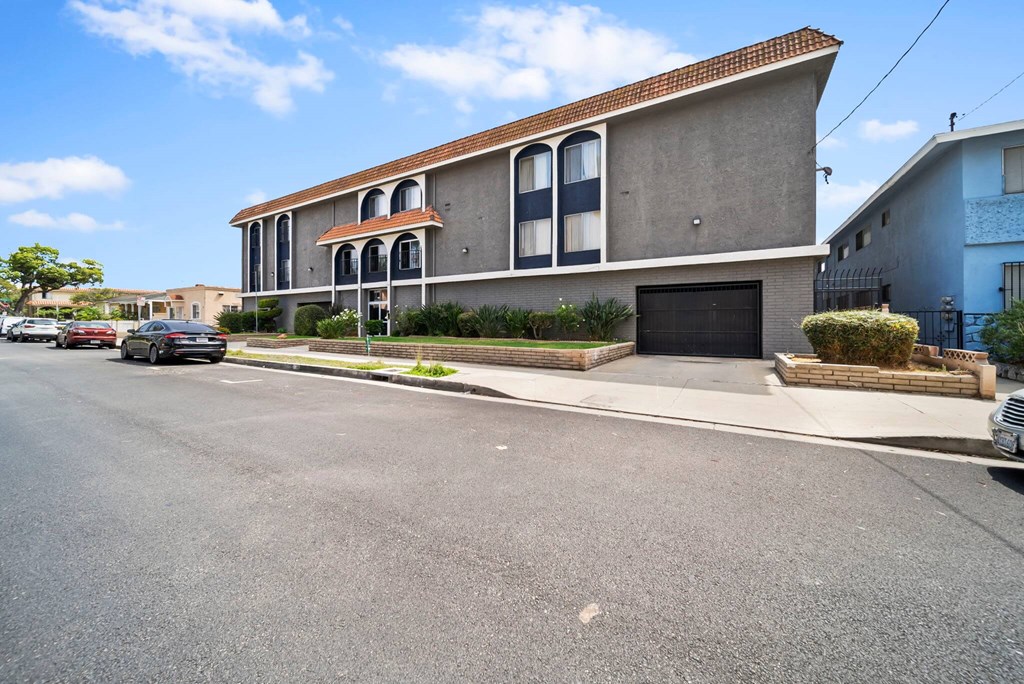 A two-story building with a red tile roof and a garage door is situated on a street with cars parked on the side.