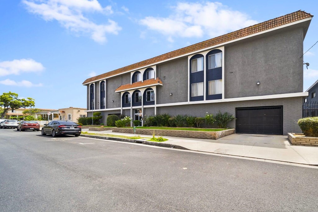 A grey building with a red roof and a black car parked in front.