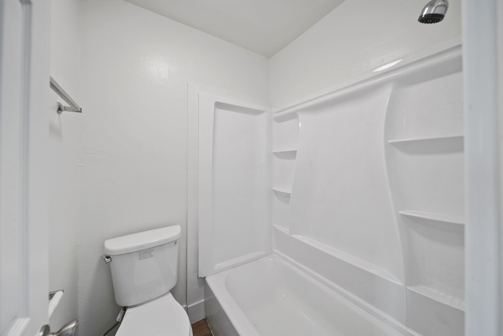 A white toilet sits next to a white bathtub in a small bathroom.