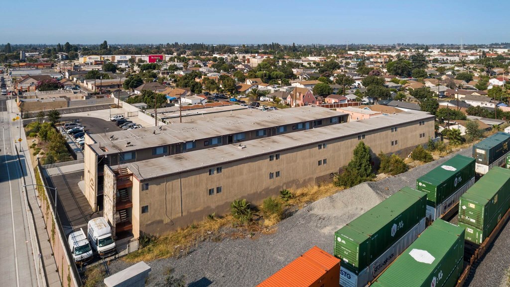 A train with green and orange containers is passing by a large building.