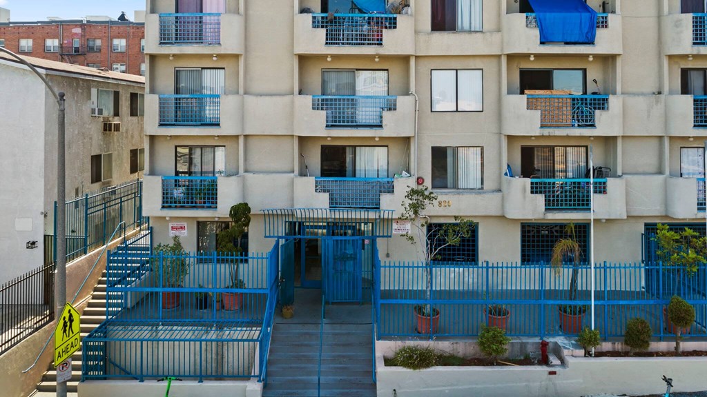A blue fence surrounds a building with a staircase leading to the entrance.